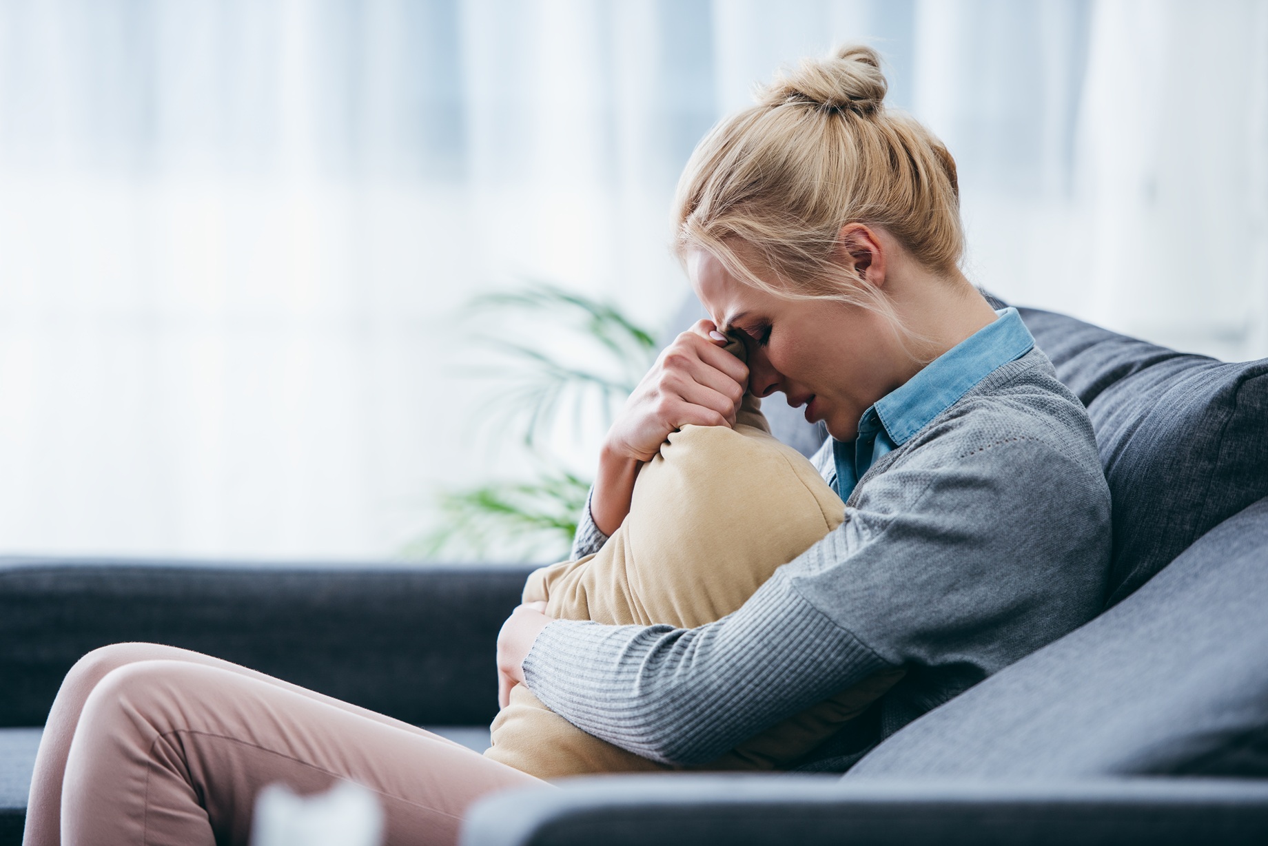 sad woman hugging pillow on couch indoors 2026