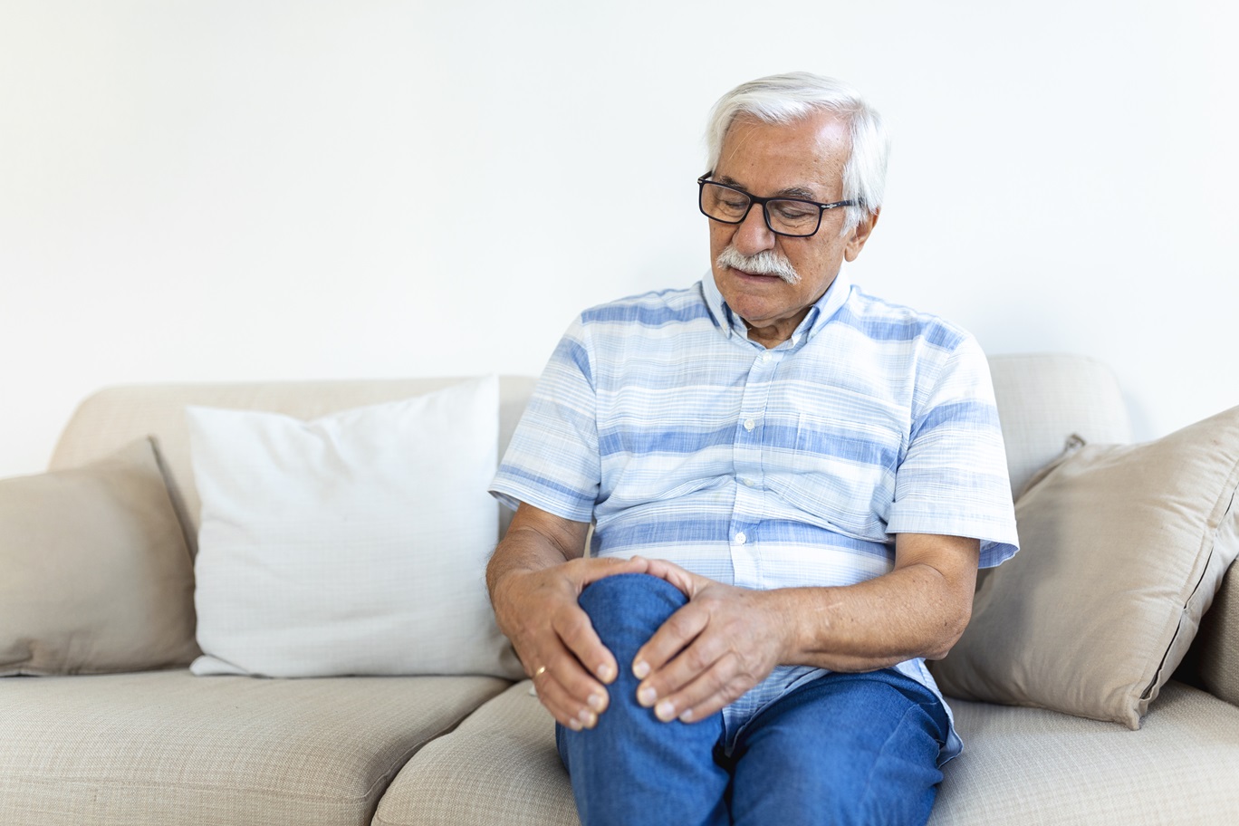 elderly man sitting sofa home touching his painful knee