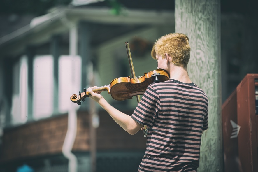 young person plays violin outdoors by building 2026